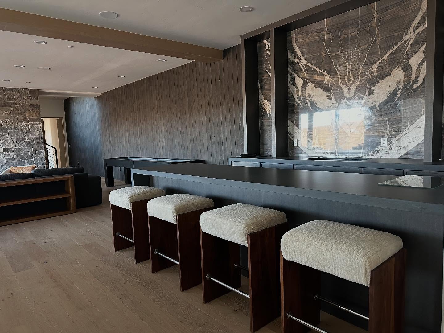 Four walnut barstools with cream shearling seats at a dark bar.