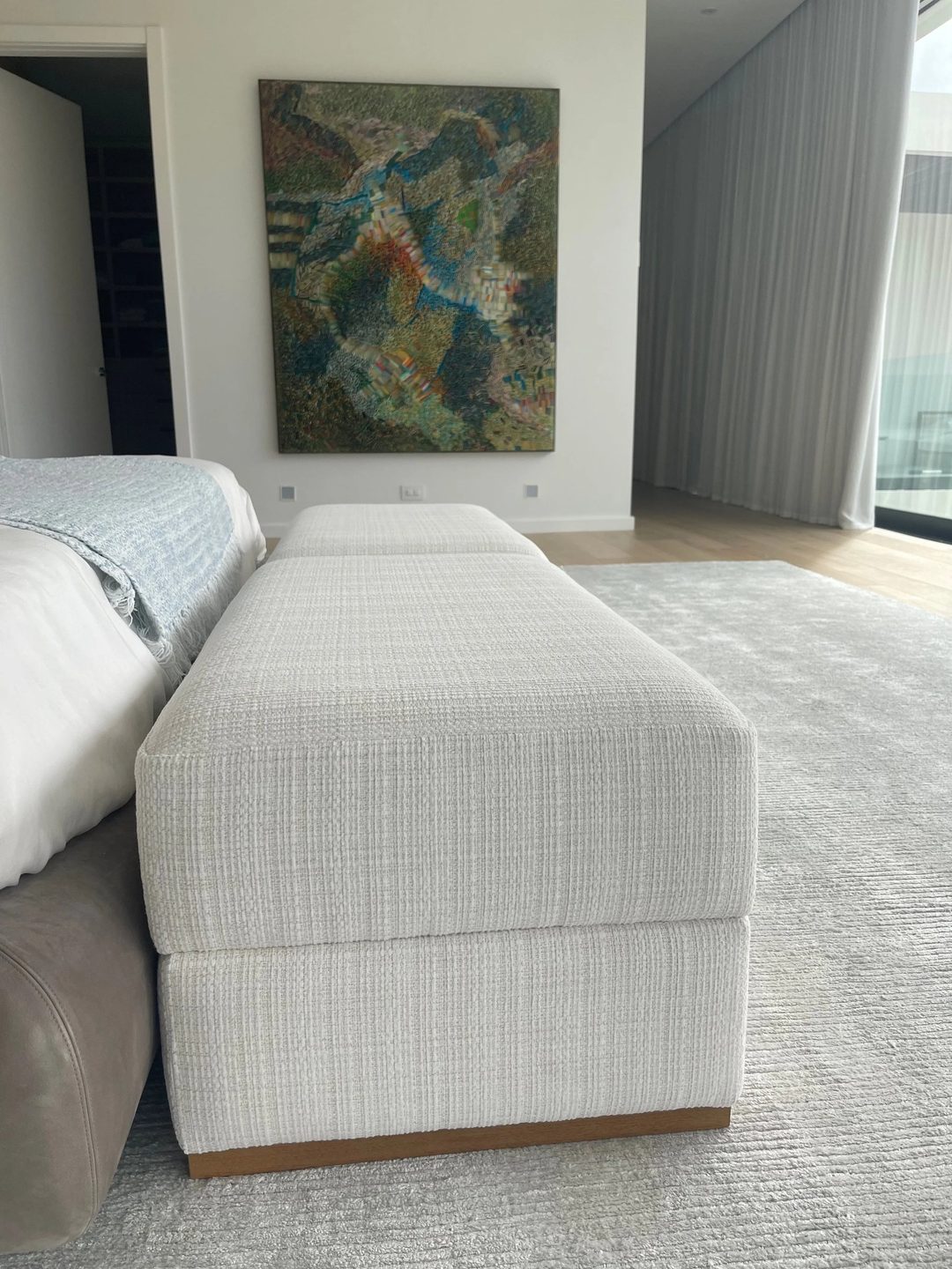 Two upholstered benches in white nubby fabric, lined up end to end at the foot of a bed, with an abstract painting on the wall beyond.