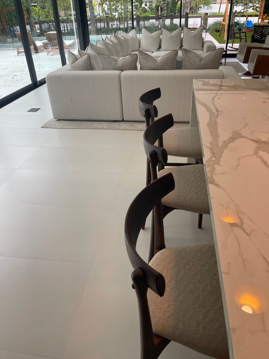 Dark wood counter stools with cream geometric-weave seats along a marble island, with a white sectional beyond.