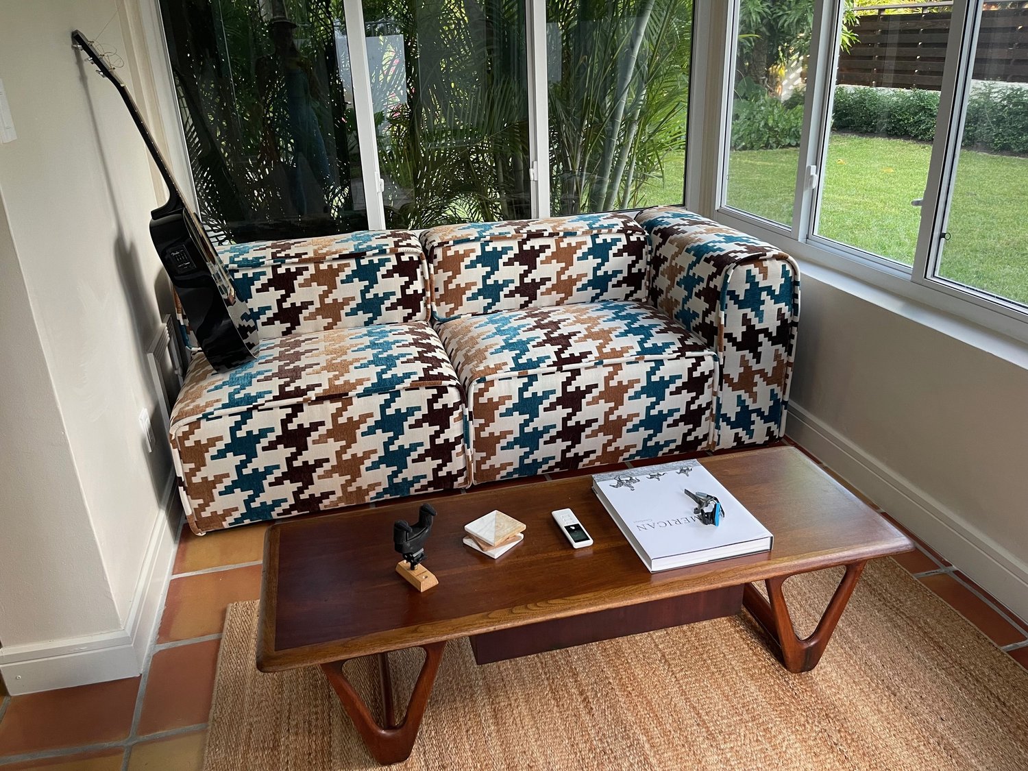 A modular loveseat in an oversized teal, brown, and tan houndstooth, in a sunroom with a wood coffee table.