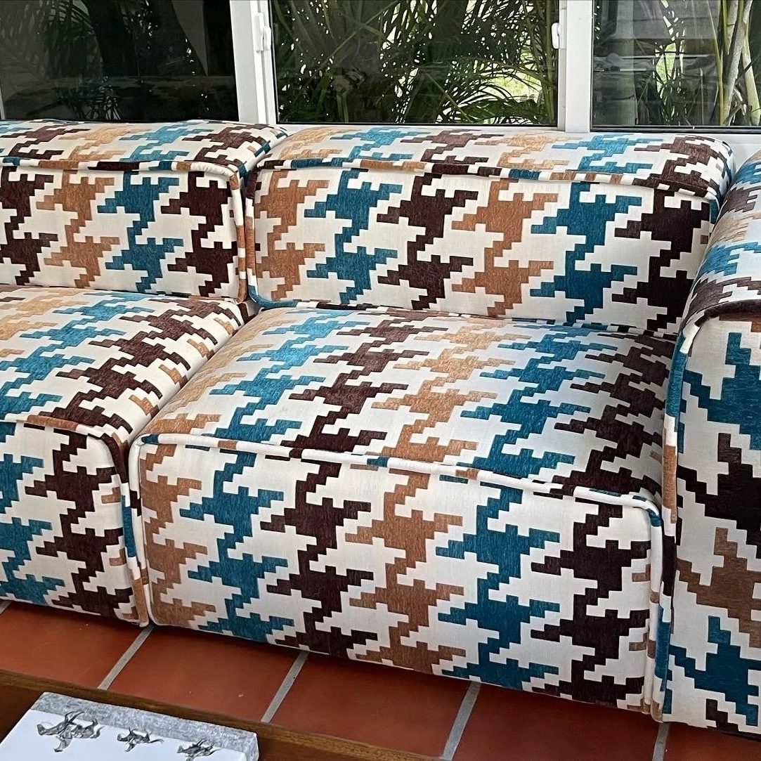 Close-up of a modular sofa in an oversized houndstooth of teal, brown, and tan on cream.