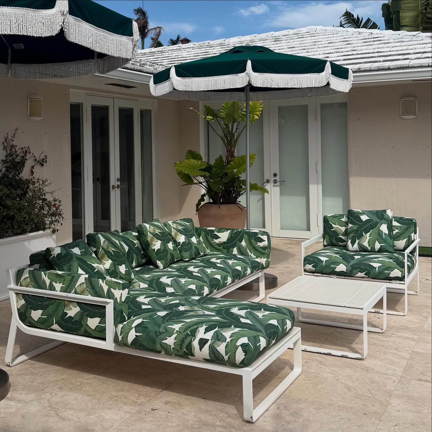 A white metal outdoor sofa and chair covered in a green palm-leaf fabric, on a Miami Beach patio.