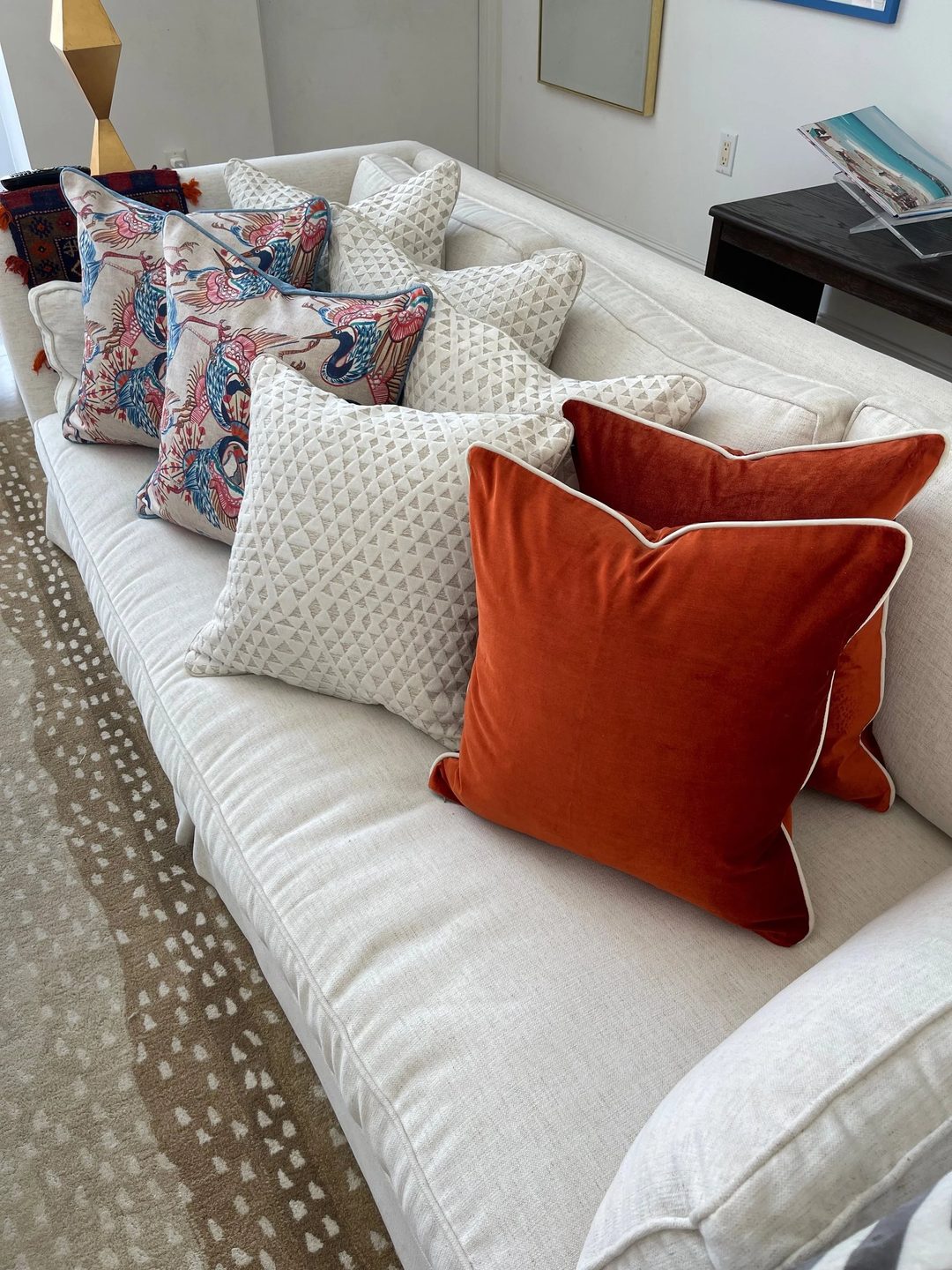 A cream sofa layered with rust velvet pillows, cream diamond-weave pillows, and pillows printed with colourful birds.
