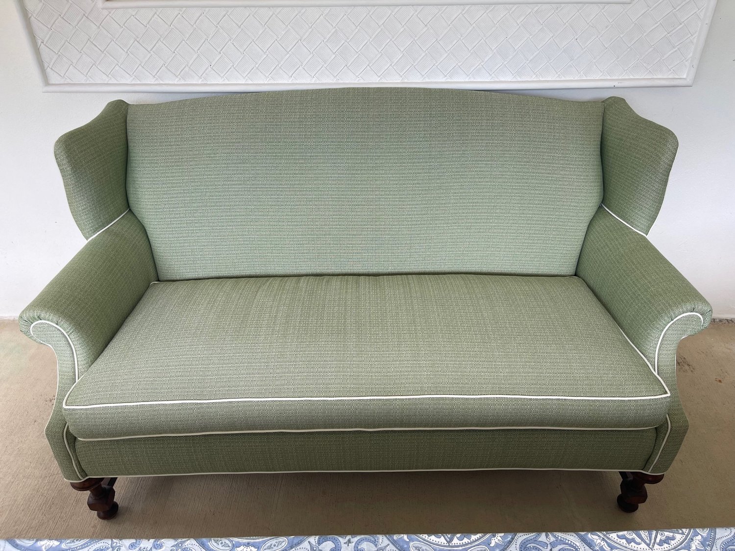 A two-seat settee in a green patterned fabric with white piping, rolled arms, and dark wood legs.