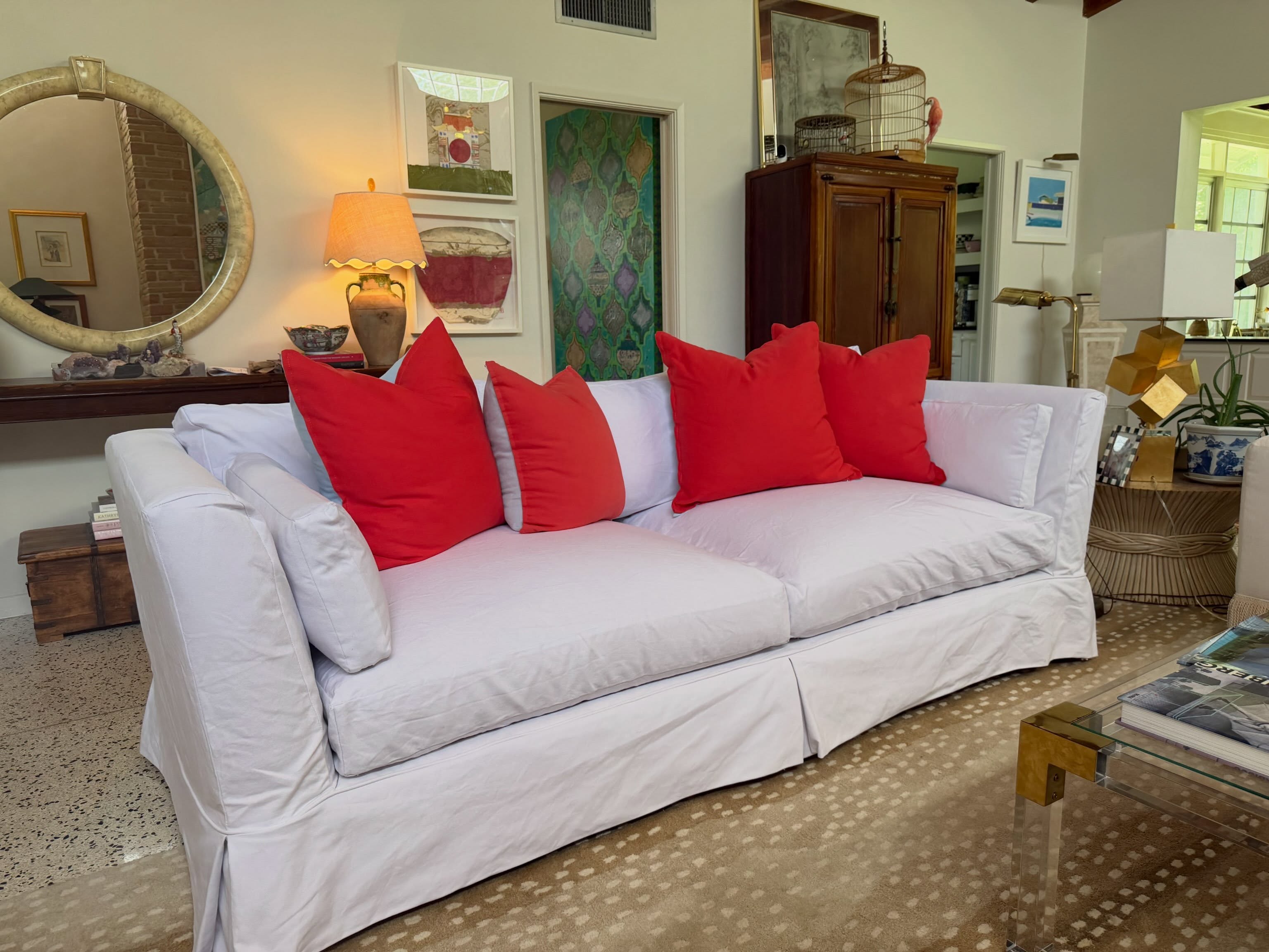 A white slipcovered sofa with four red throw pillows in a furnished living room.