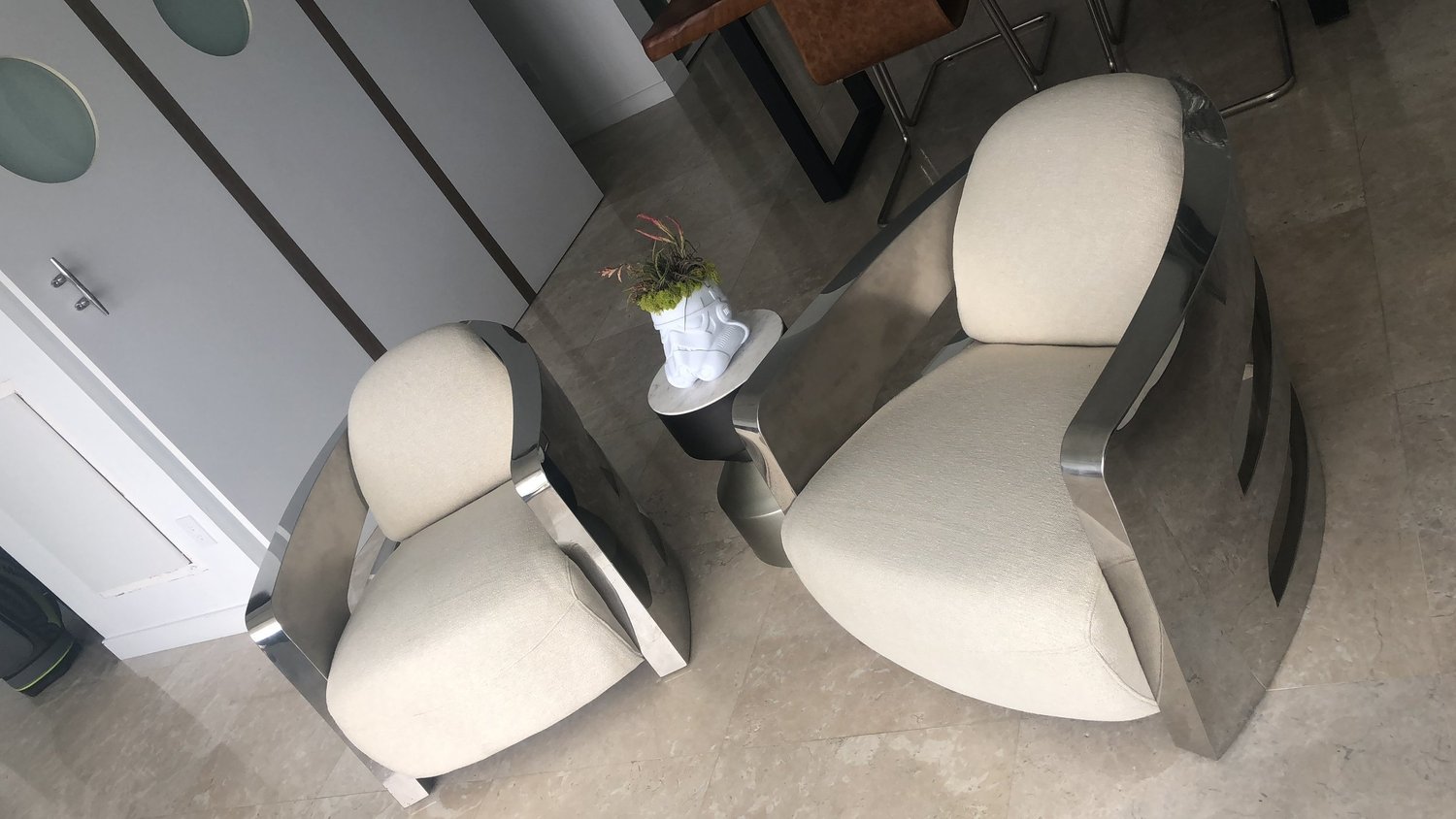 Two chrome-framed lounge chairs with sand-coloured upholstered seats and backs, seen from above.