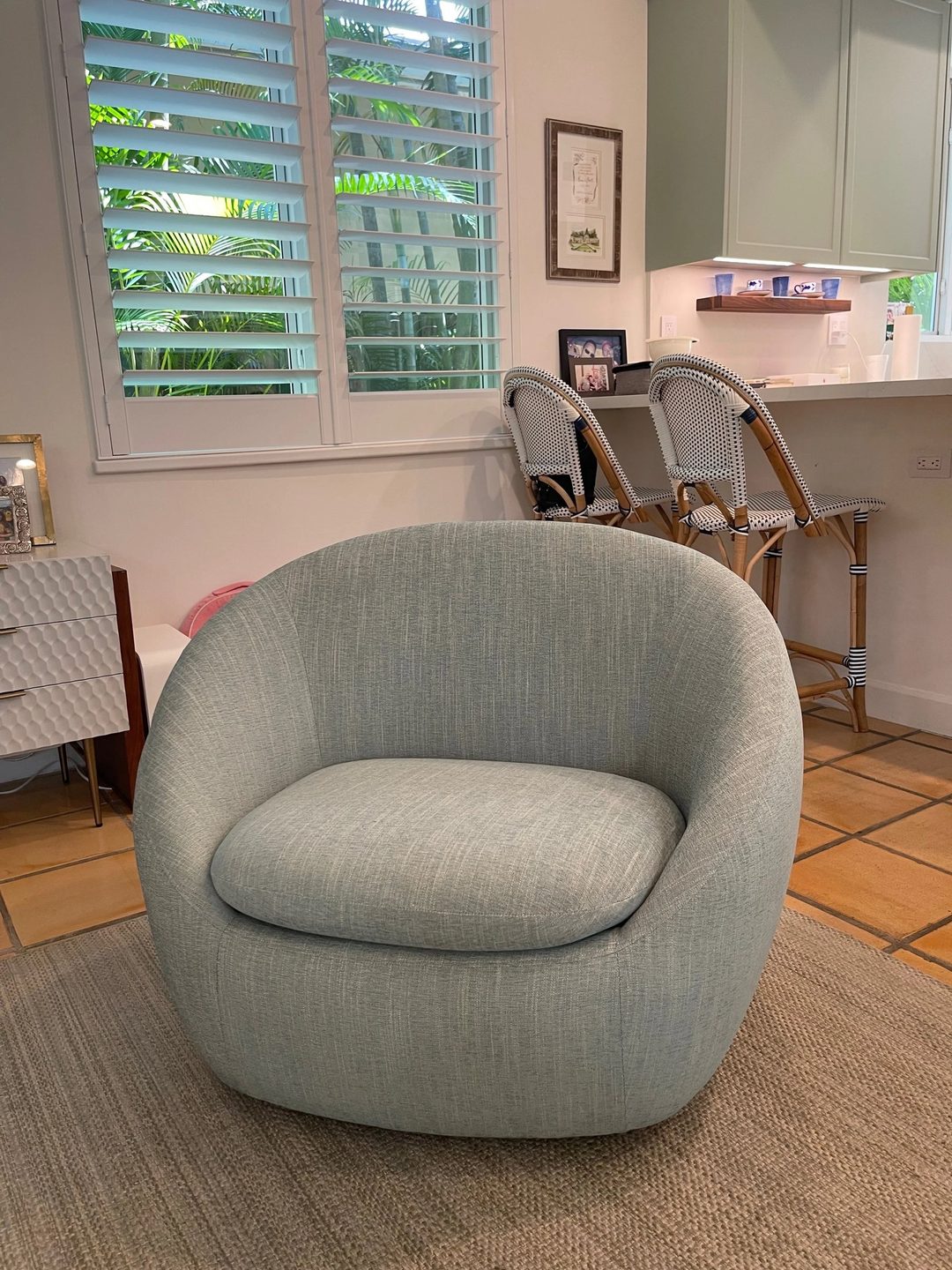 A rounded barrel chair in a pale seafoam weave on a sisal rug, in a kitchen.