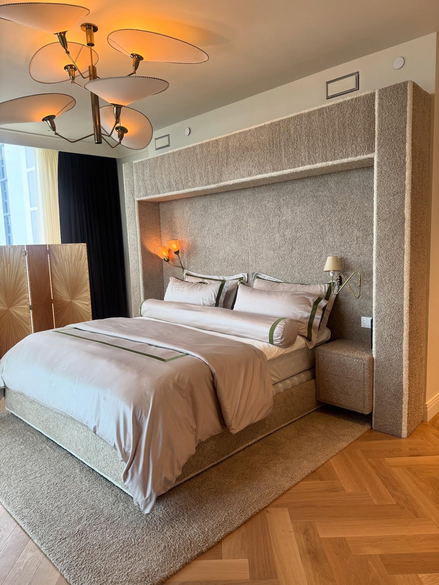 A custom bed set into a boucle wall unit, with a boucle nightstand and a sculptural ceiling light.